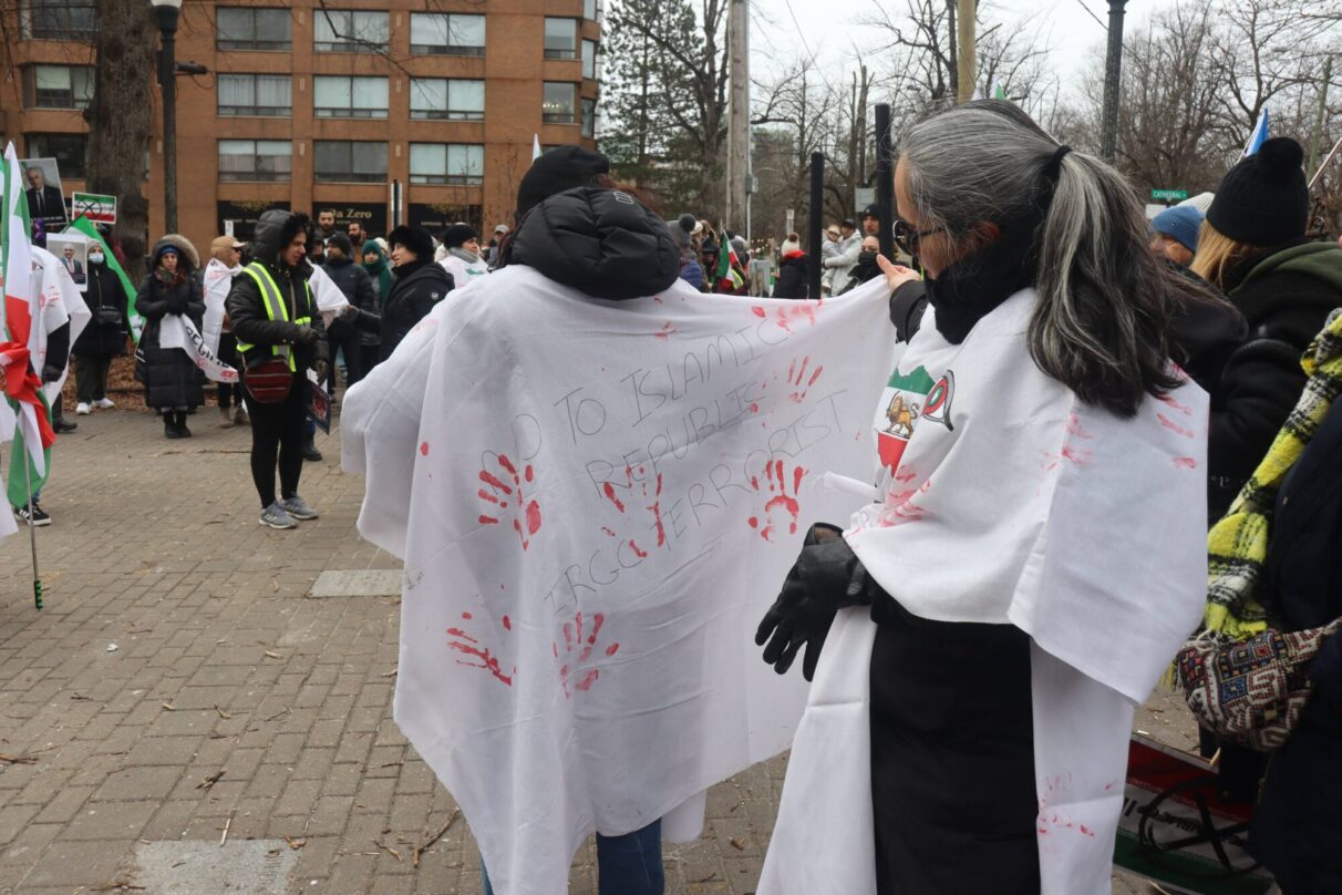 Ziba Mashkori, right, holds up a cover with "No to Islamic Republic," and "IRGC Terrorist" written on the back.