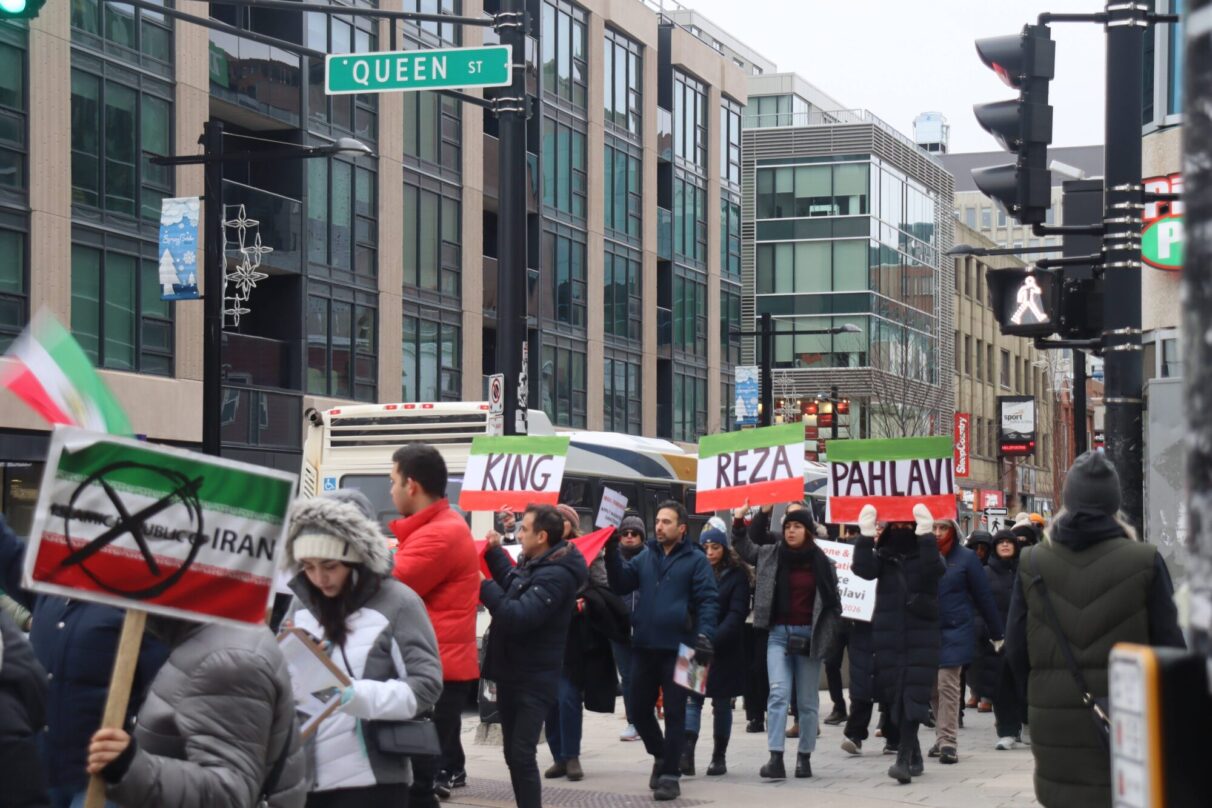 Protesters holding up signage saying "King Reza Pahlavi" while walking down Queen St, Halifax.