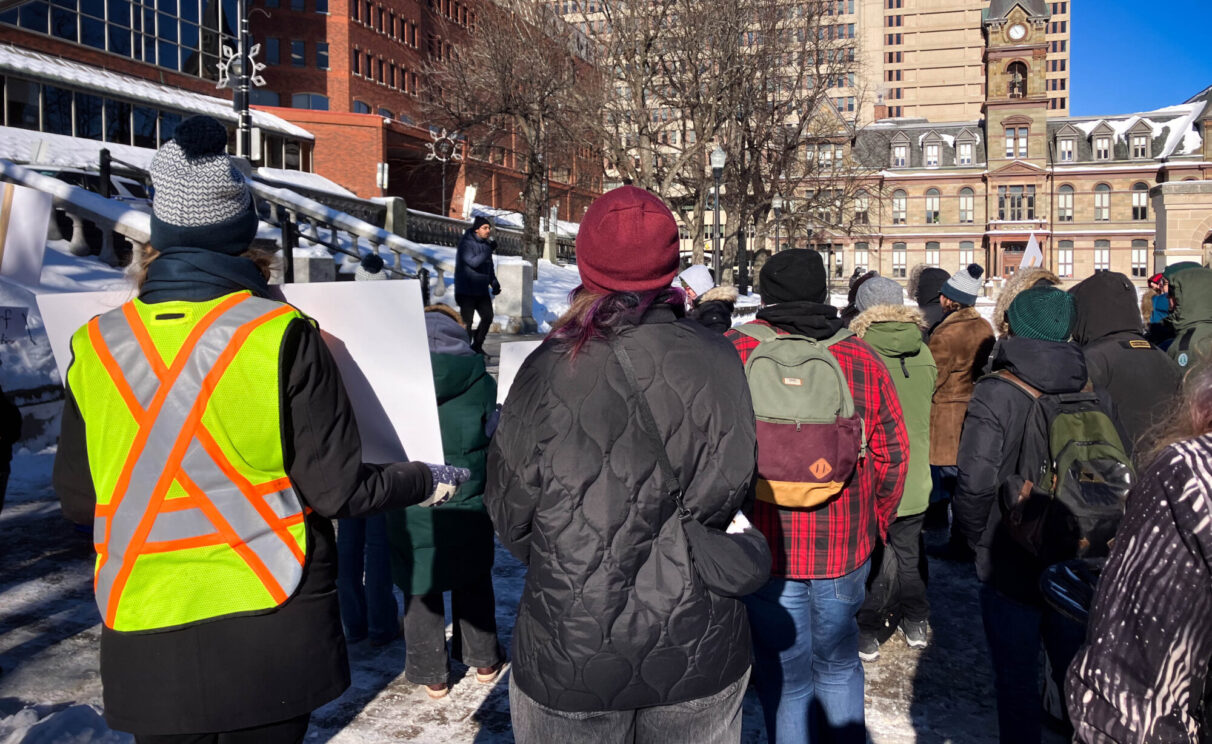 Rally attendees stand and listen to a speaker on the steps of Grand Parade.