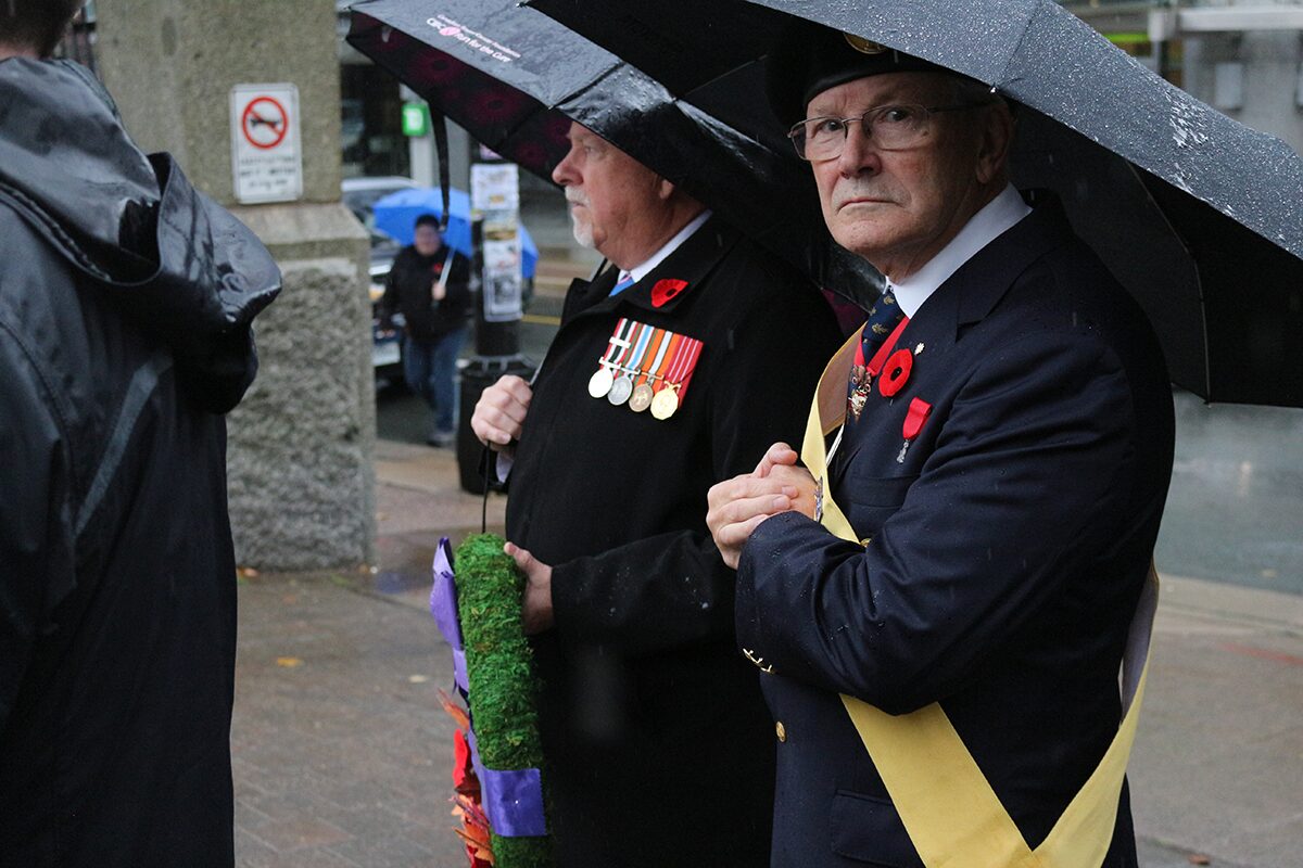 Two elderly male veterans holding umbrellas and carrying a wreath enter the Halifax Grand Parade for the 2024 Remembrance Day ceremony.