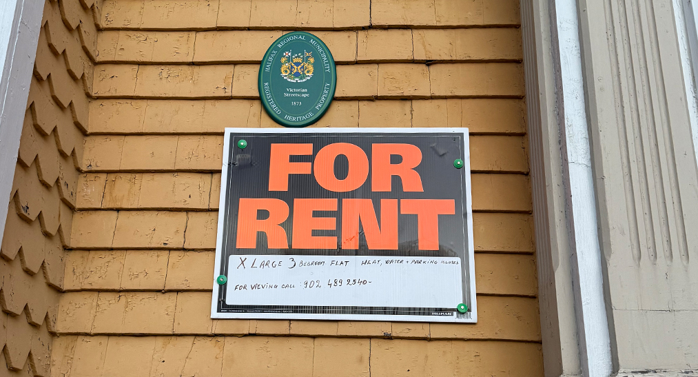 For Rent sign nailed to yellow wooden siding of a house.