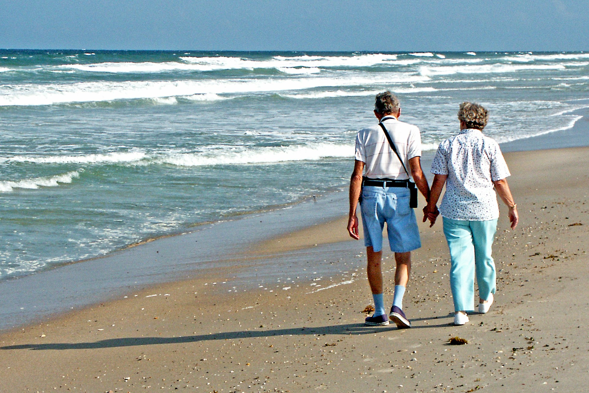 A senior couple walk hand-in-hand on a beach.