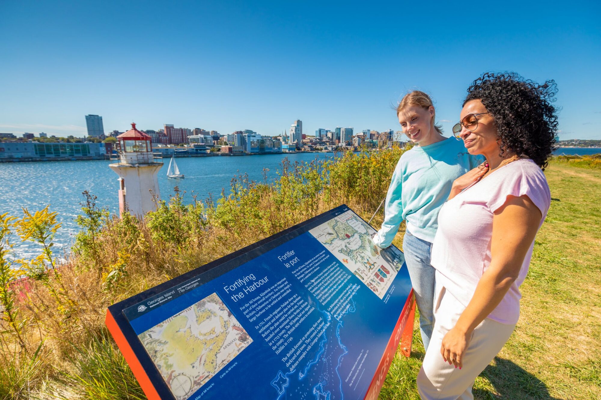 Visitors are reading a plaque at Georges Island National Historic Site in Halifax explaining the significance of the site historically.