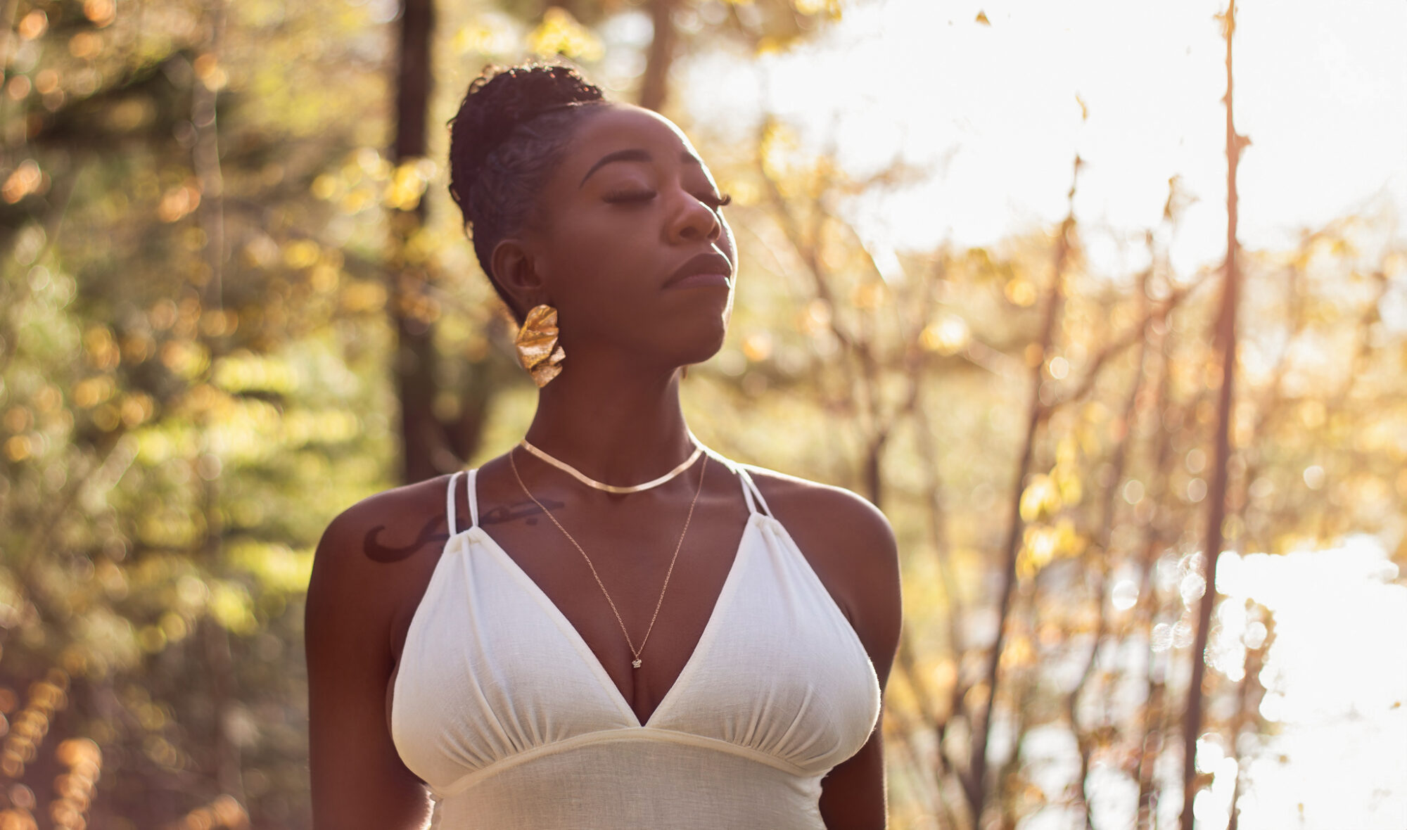 Jhamiela Smith looking into the sun with trees in the back, and wearing a white dress