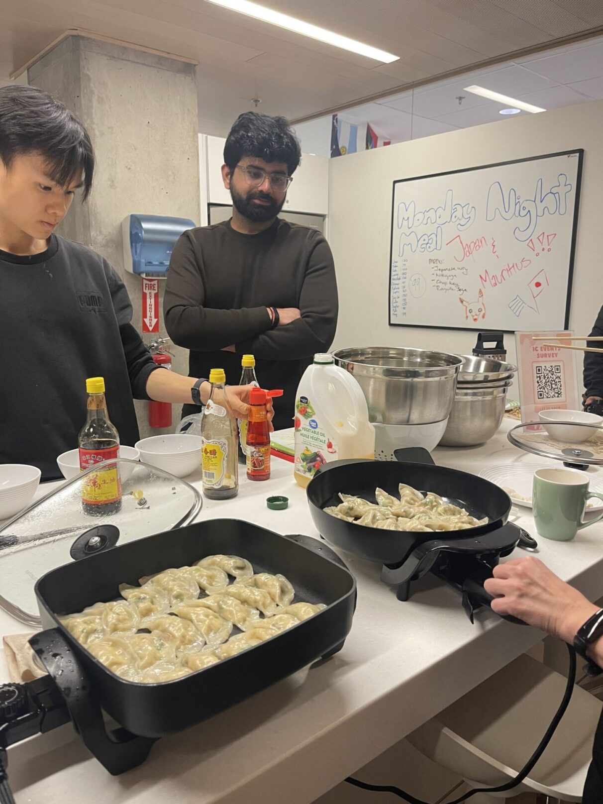 Two students infront of the pans of dumplings being cooked