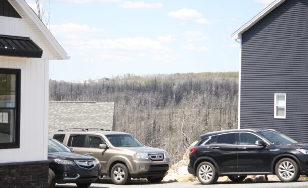 Three cars sit in between two houses. Scorched trees are in the background, showing how close forest fires get to neighbourhood infrastructure.