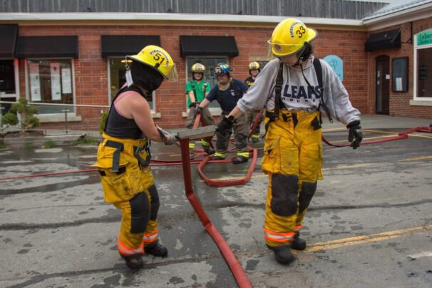 Two firefighters roll out a fire hose in the parking lot in front of a business.